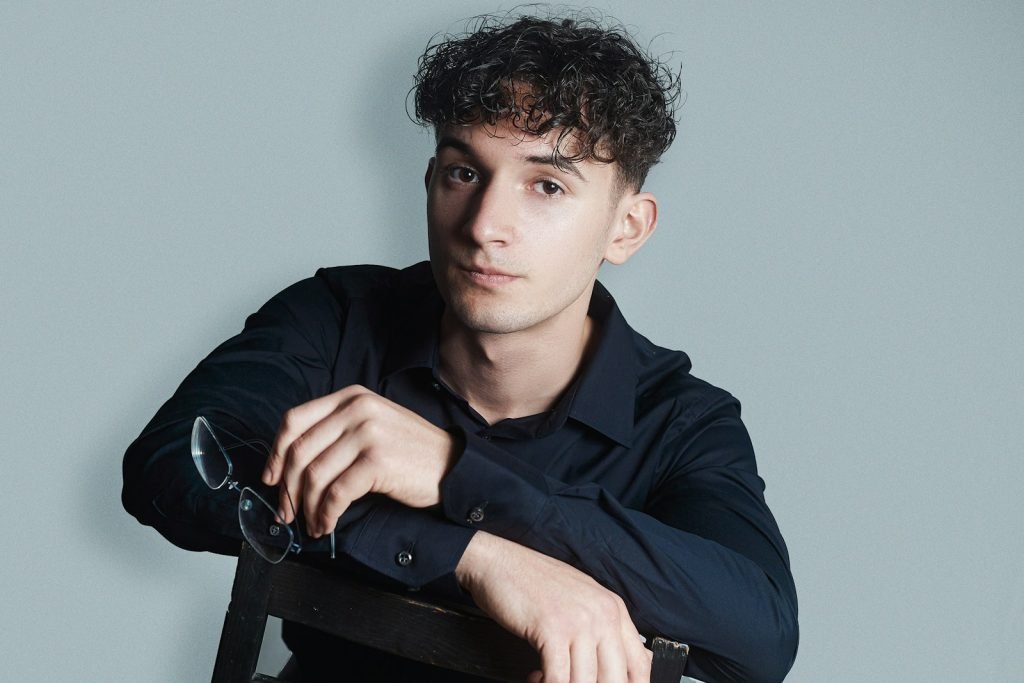 a young man sitting in a chair holding a pair of glasses